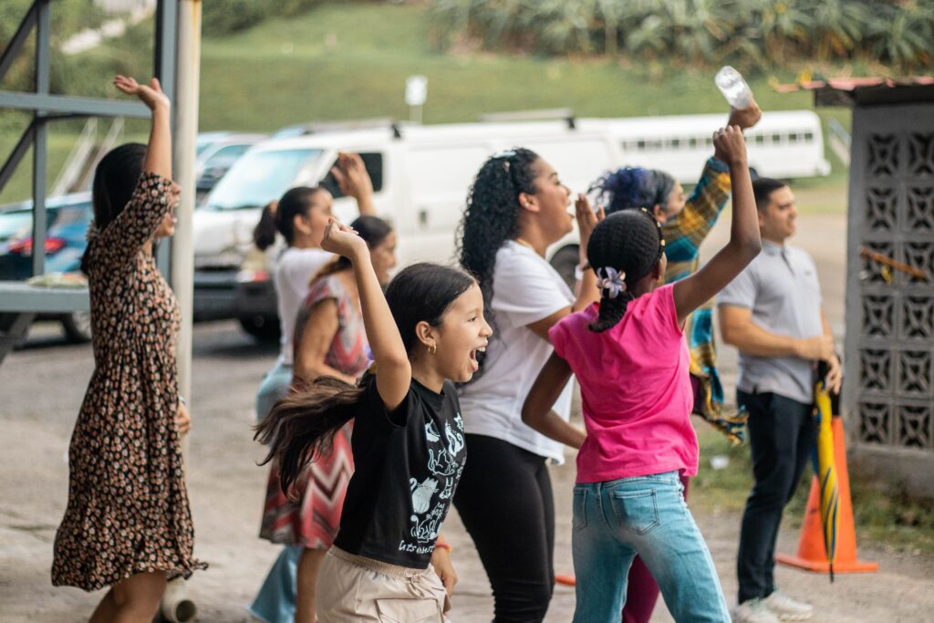 A joyful group of diverse people celebrating with raised arms in an outdoor setting.