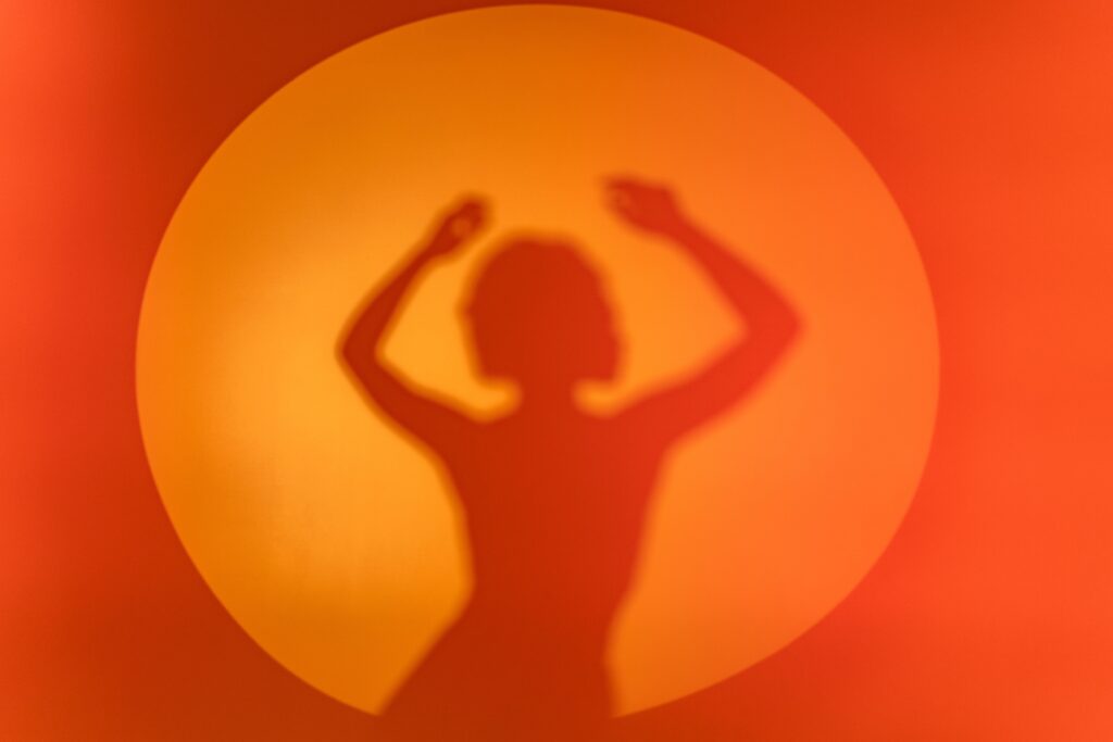 A silhouette of a woman's shadow dancing against a vibrant orange circular background.